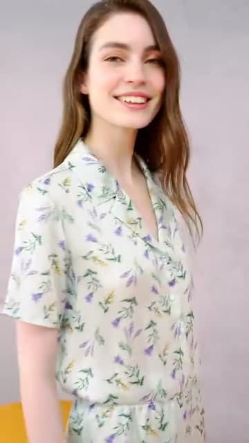 A model in sage floral pyjamas smiling against a blush backdrop.